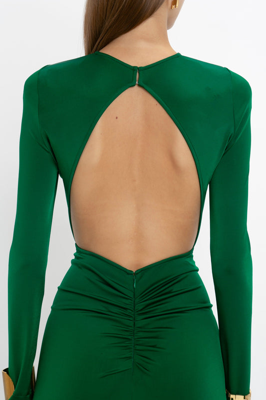 A woman in a green, body-sculpting Circle Detail Open Back Gown In Emerald by Victoria Beckham with long sleeves and an open back design stands with her back to the camera.