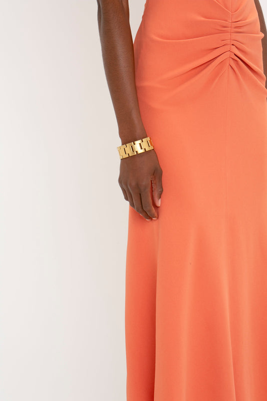 Close-up of a person wearing a Victoria Beckham Gathered Waist Midi Dress In Papaya and a golden bracelet.