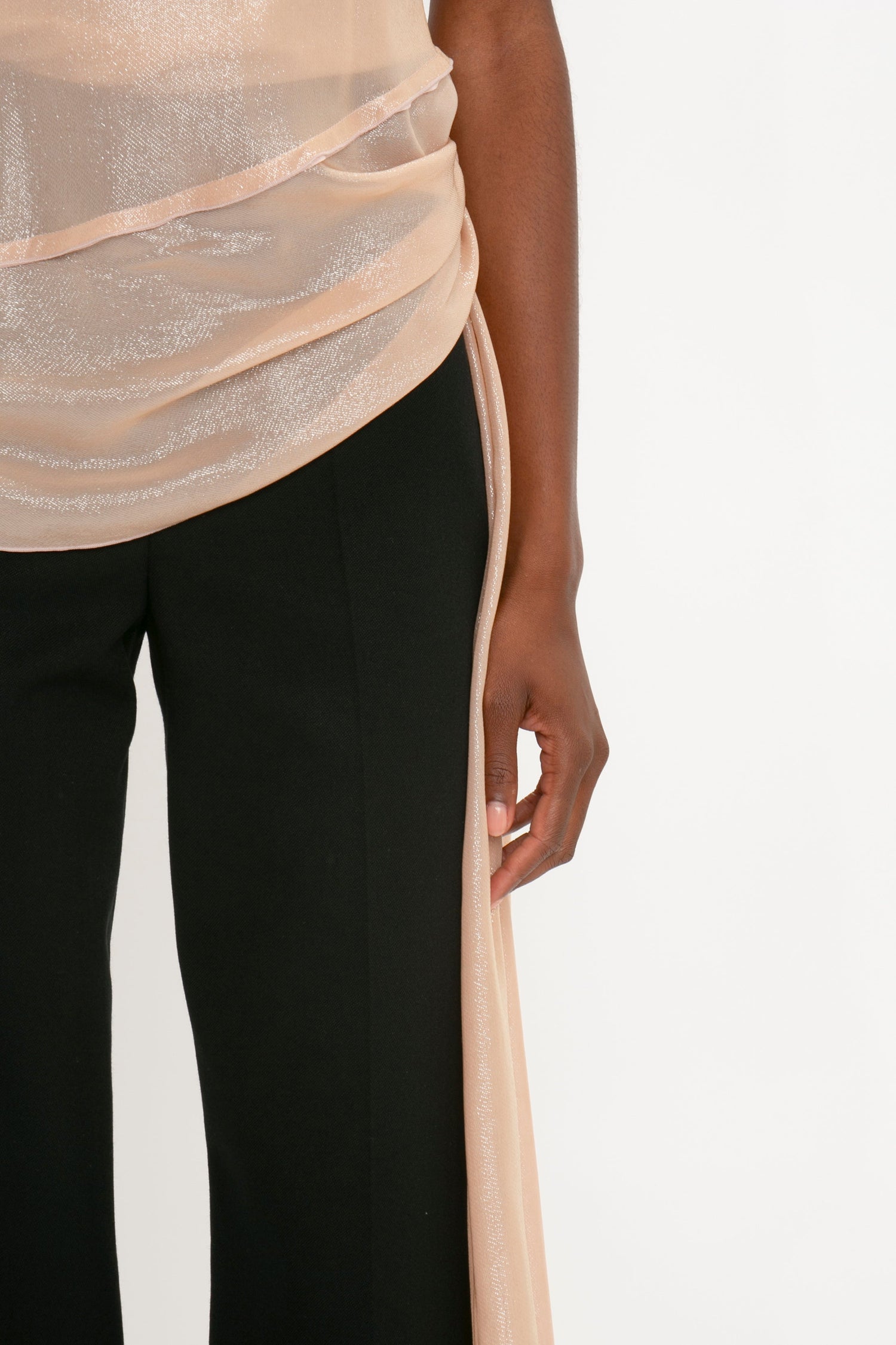 Partial view of a person wearing a shimmering beige halter top with draped fabric and black Satin Panel Straight Leg Trousers, standing against a plain white background.

Revised Sentence:
Partial view of a person wearing a Flower Detail Cami Top In Rosewater by Victoria Beckham with draped fabric and black Satin Panel Straight Leg Trousers, standing against a plain white background.