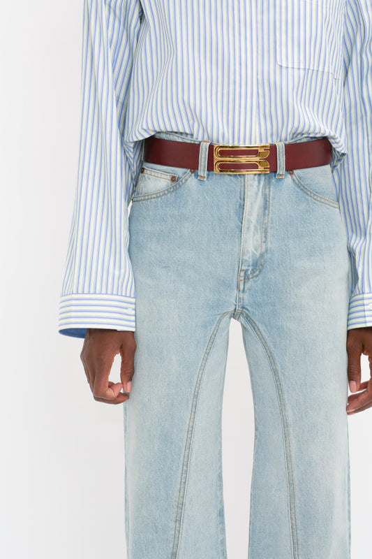 Torso of a person wearing blue striped Button Detail Cropped Shirt, Victoria Beckham's Bianca Jean In Light Blue Denim jeans, and a red belt with a gold buckle.