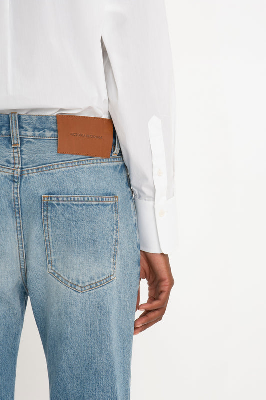 Rear view of a person wearing a classic white "Victoria Beckham" Cropped Long Sleeve Shirt tucked into blue jeans with a visible brown "Victoria Beckham" brand label on the jeans' waistband.
