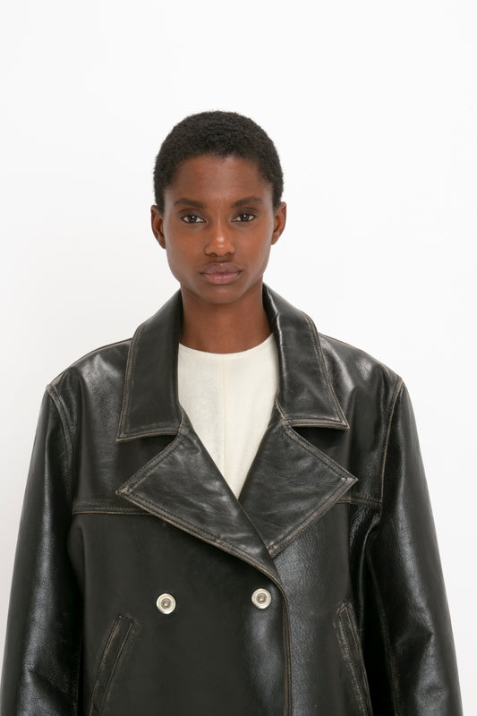 A person with short hair is wearing an Oversized Leather Jacket In Black by Victoria Beckham made of 100% calf leather and a white shirt, standing against a plain white background.
