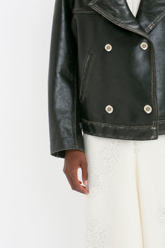A person wearing an Oversized Leather Jacket In Black by Victoria Beckham and white pants stands against a plain white background.