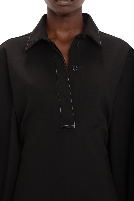 Close-up of a person wearing the Victoria Beckham Waistcoat Detail Ponti Top In Black with white stitching and a partially buttoned placket, showcasing a distinctive personality. The background is plain white.