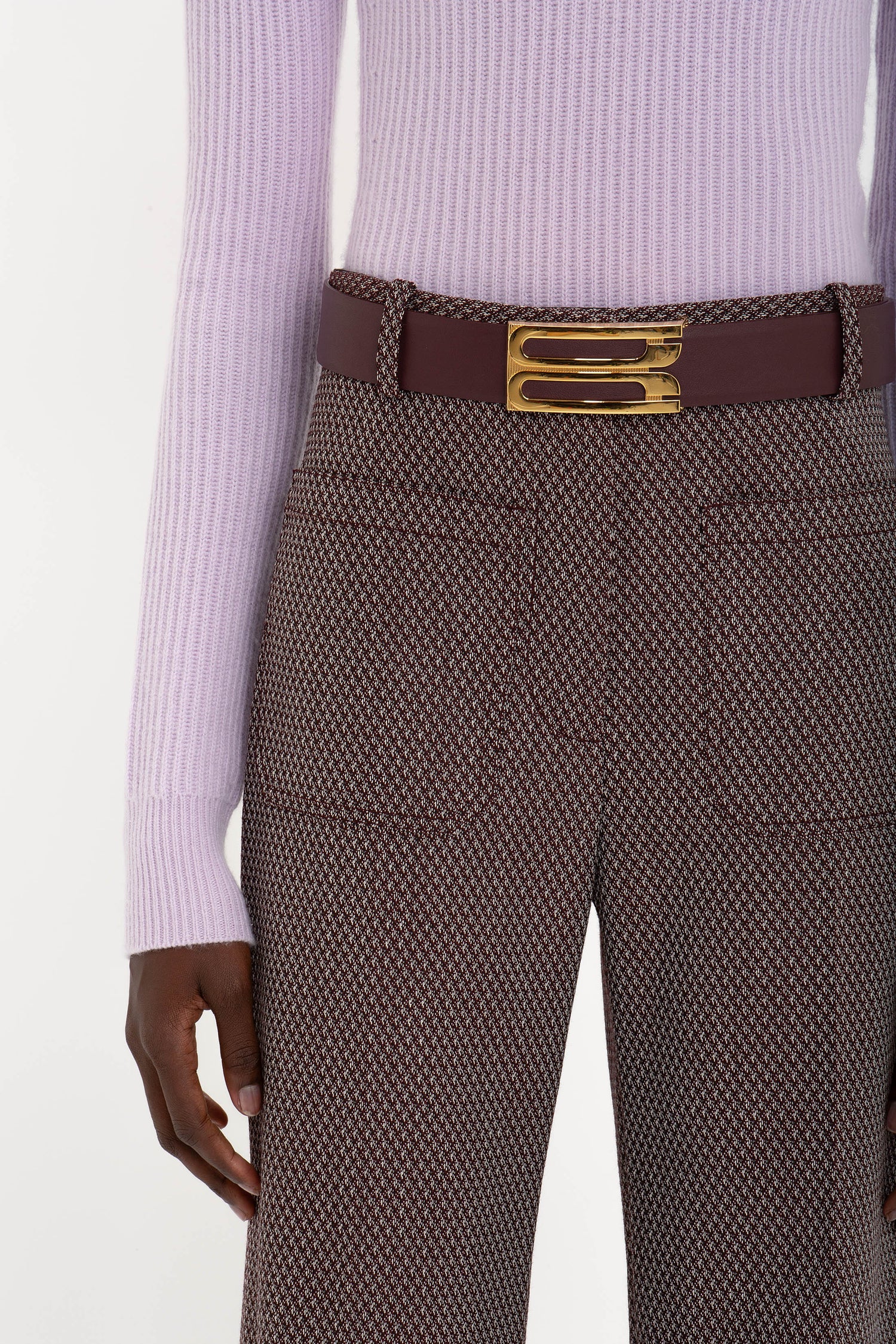 Person in a Victoria Beckham Double Collared Jumper In Petunia and patterned pants with a burgundy belt featuring a gold buckle.