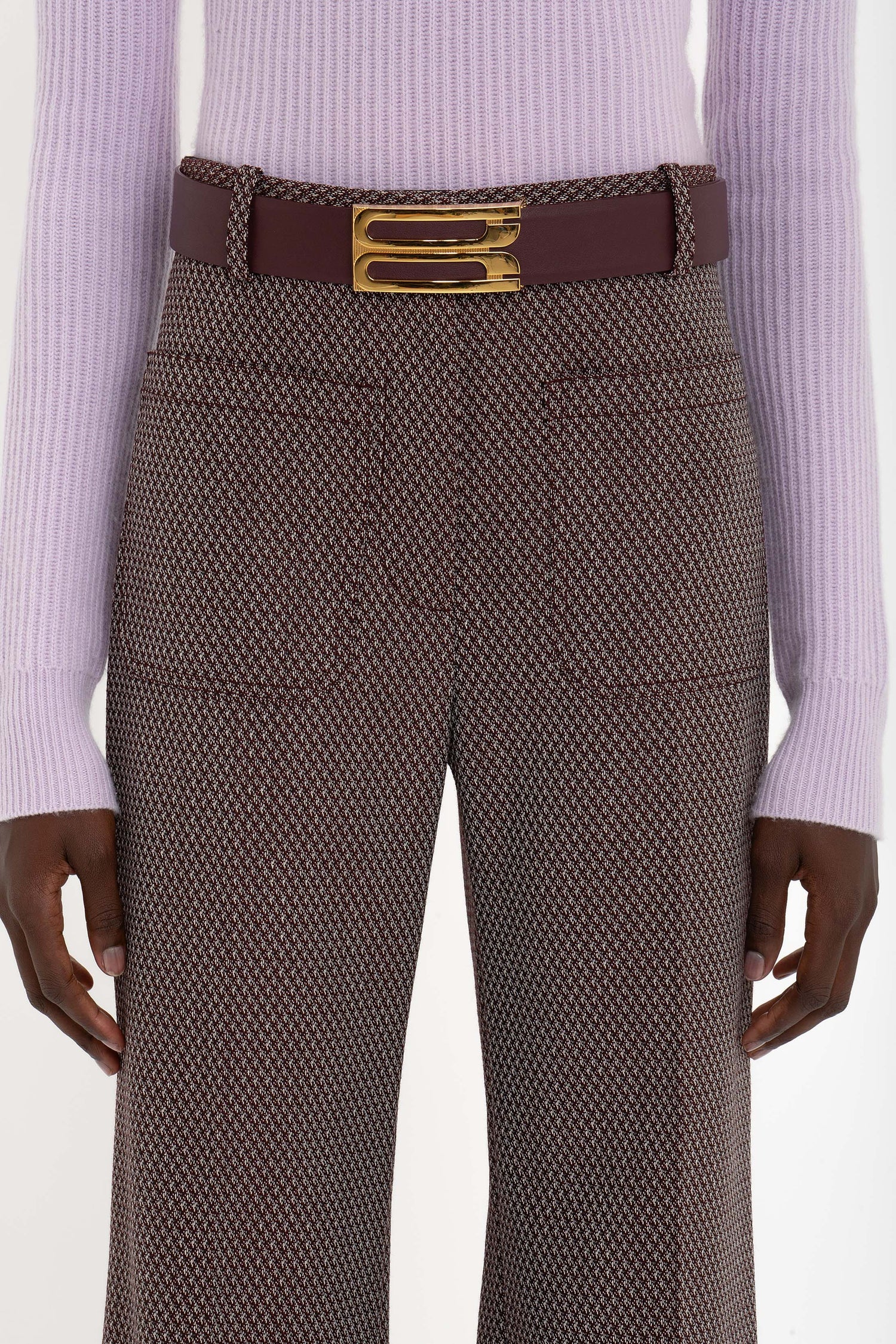 A person wearing a lilac ribbed sweater, Victoria Beckham's Alina Trouser In Tobacco with a structured design, and a dark brown belt with a gold buckle.