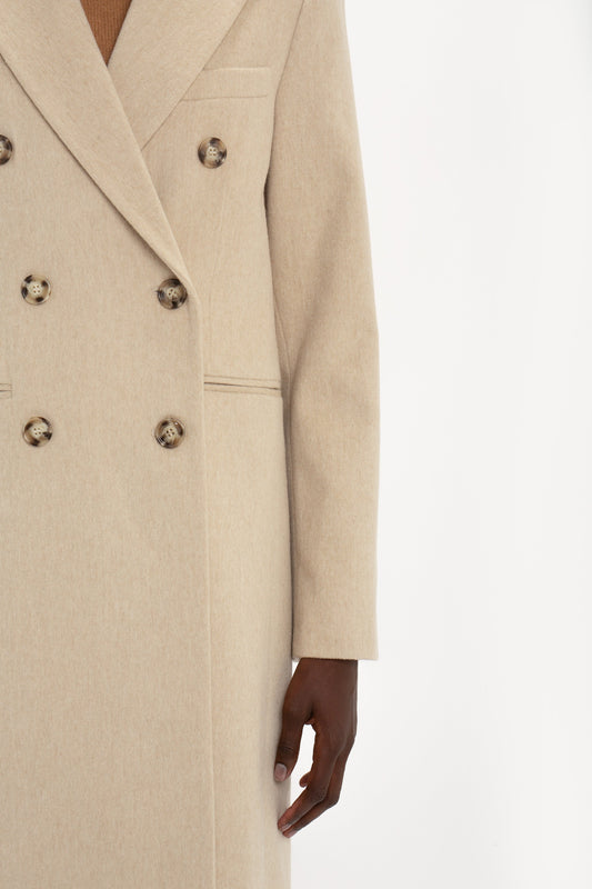 Person wearing a light beige **Tailored Slim Coat In Bone** by **Victoria Beckham** with tortoiseshell buttons. Only the torso and one arm are visible.