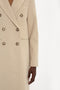 Person wearing a light beige **Tailored Slim Coat In Bone** by **Victoria Beckham** with tortoiseshell buttons. Only the torso and one arm are visible.