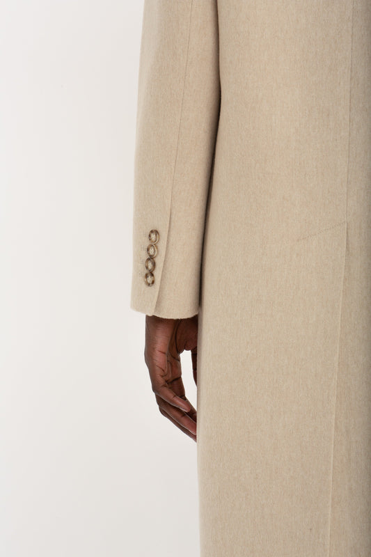 A close-up of a person wearing the Victoria Beckham Tailored Slim Coat In Bone with four buttons on the sleeve. The person's hand is partially visible, resting against their side.