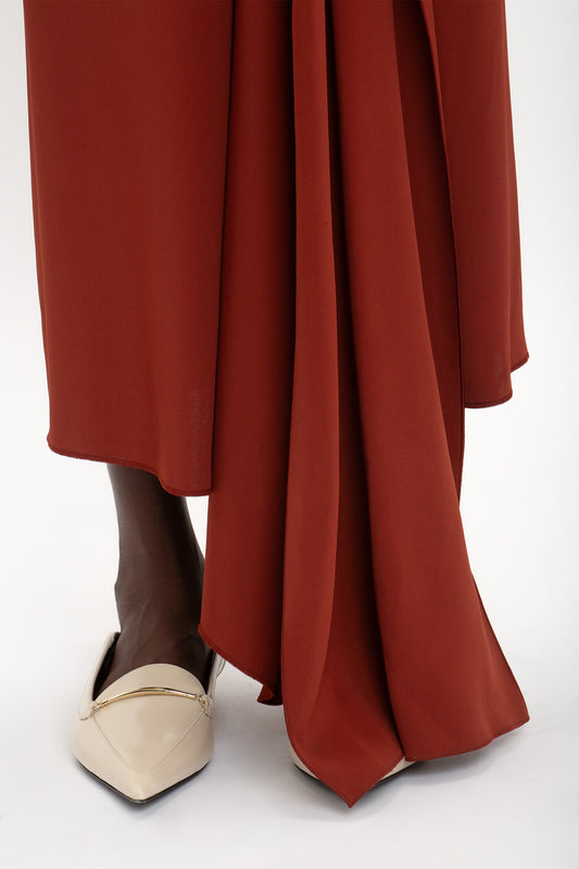 Close-up of a person wearing the Victoria Beckham High Neck Tie Detail Dress In Russet with an asymmetric hemline and beige pointed-toe flats.