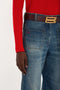 Close-up of a person wearing a Victoria Beckham Polo Neck Jumper In Red, dark red belt with a gold buckle, and blue jeans with "AG" embroidered on the pocket.