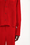 A person wearing a red button-front shirt and matching red pants. The image shows the upper half of the body from the neck down, with the shirt featuring a chic cropped length style reminiscent of Victoria Beckham's Cropped Long Sleeve Shirt In Carmine designs.