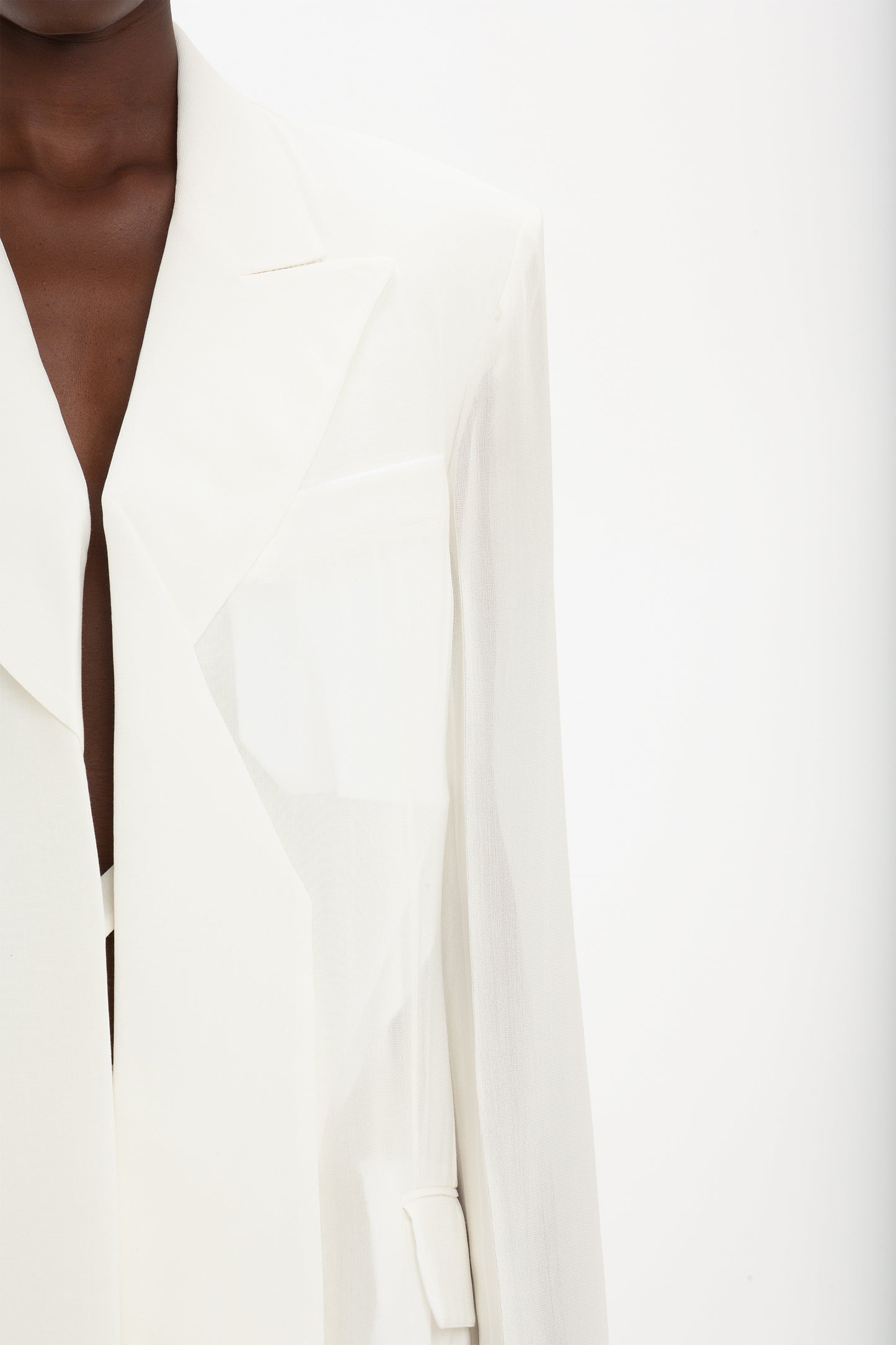 Close-up of a person wearing a white, Fold Detail Tailored Jacket In White by Victoria Beckham made from featherweight wool with a wide lapel against a plain white background. Only part of their face and upper body are visible, giving the ensemble a modern flair.