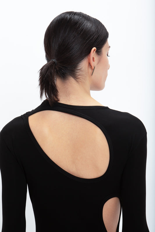 A person with dark hair tied back wears a sleek, black Cut-Out Jersey Floor-Length Dress In Black from Victoria Beckham, seen from behind against a white background.