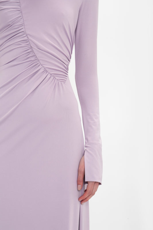 A close-up of a person's torso wearing a long-sleeved, lavender-colored Ruched Detail Floor-Length Gown In Petunia by Victoria Beckham. The understated glamour is evident as the person's arm rests by their side.