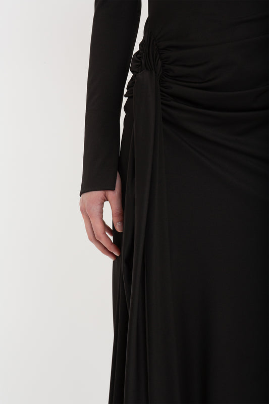 Close-up of a person wearing a Victoria Beckham High Neck Asymmetric Draped Dress In Black with a detailed knot design on the side, set against a white background.