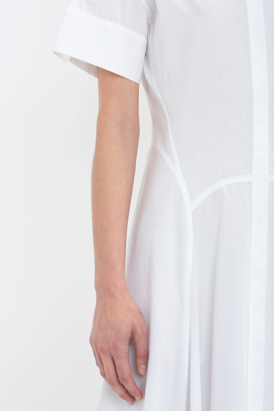 Close-up of a person wearing a Victoria Beckham Panelled Shirt Dress In White crafted from organic cotton poplin. The image focuses on the side of the dress and the person's arm, highlighting the tailored design.