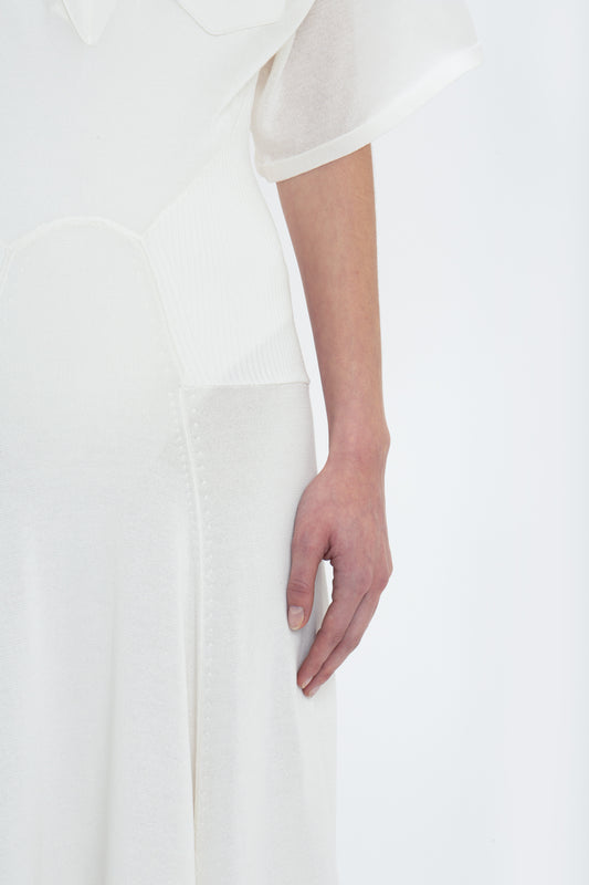 A person in a Victoria Beckham Panelled Knit Dress In White with a visible hand resting against the side of the lightweight garment. The background is plain white, exuding an air of relaxed glamour.
