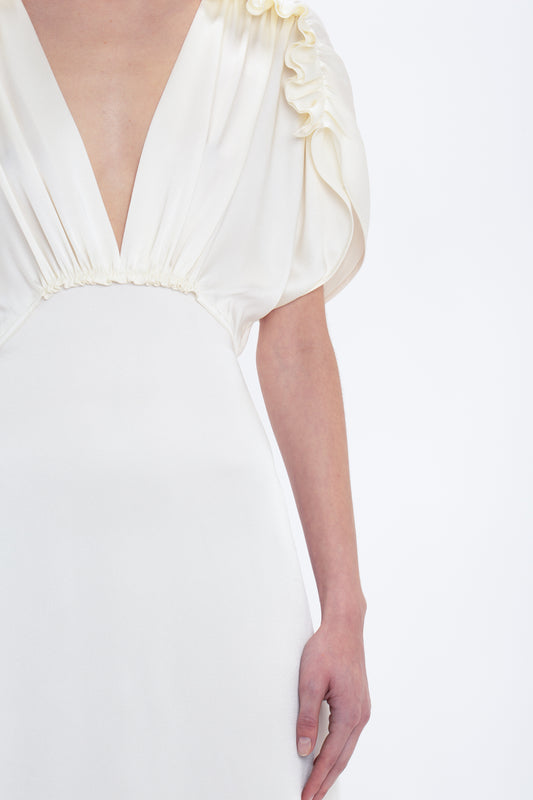 A person is wearing a white Exclusive V-Neck Ruffle Midi Dress In Ivory with a deep V-neckline and gathered short sleeves, shown from chest to hip level against a plain white background, reminiscent of Victoria Beckham's chic aesthetic.