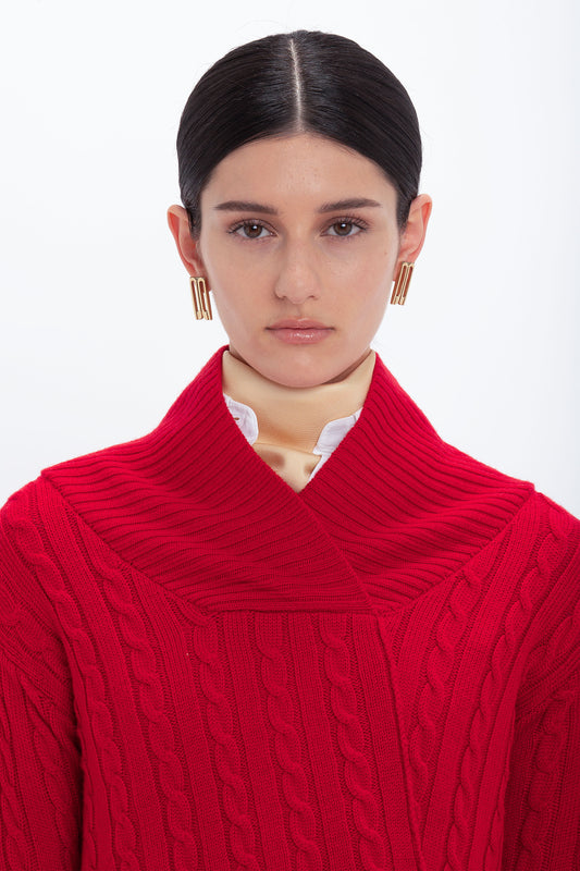 A person with dark hair and gold earrings is wearing a Wrap Detail Jumper In Red from the Victoria Beckham brand over a white shirt, looking directly at the camera against a plain white background.