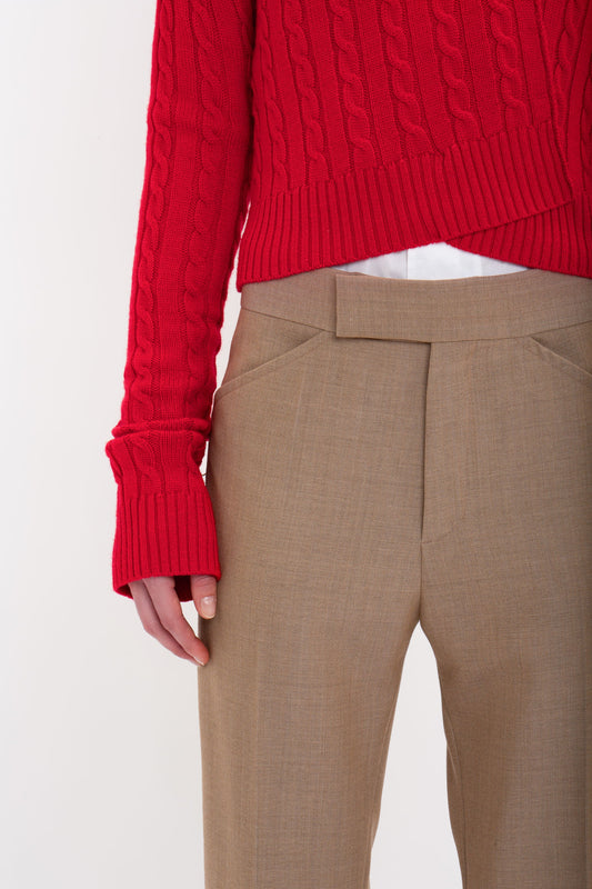 A person wearing a red cable-knit sweater and flattering Victoria Beckham Wide Cropped Flare Trouser In Tobacco stands against a white background.