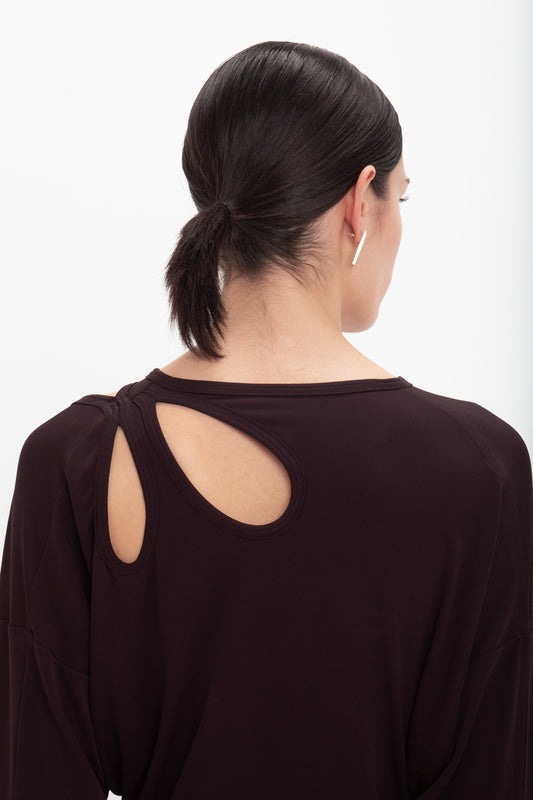 A person with dark hair tied in a low ponytail, wearing a Twist Detail Jersey Top In Deep Mahogany by Victoria Beckham, effortlessly exudes casual sophistication.