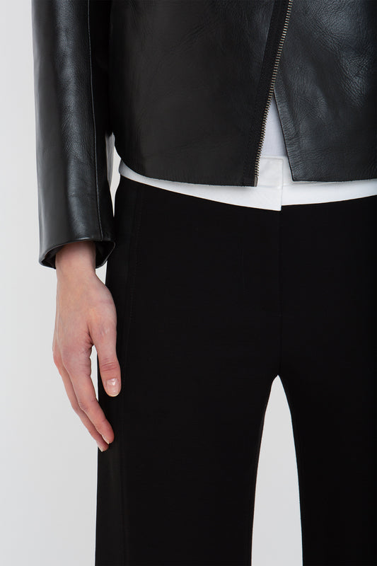 A person is dressed in a black **Victoria Beckham Tailored Leather Biker Jacket In Black** over a white shirt and black pants, with their hand resting at their side, exuding a modern classic vibe.