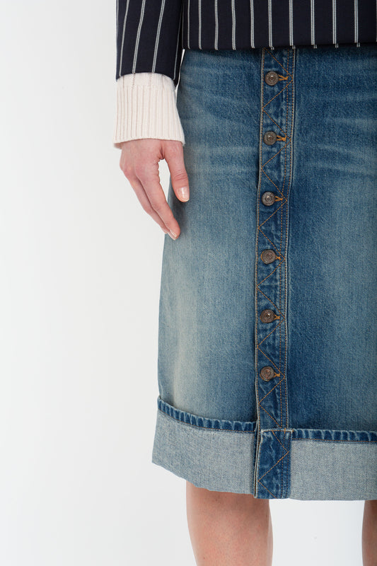 Person wearing a pinstripe top with cream-colored cuffs and a Victoria Beckham Placket Detail Denim Skirt in Heavy Vintage Indigo Wash featuring an asymmetric front placket.