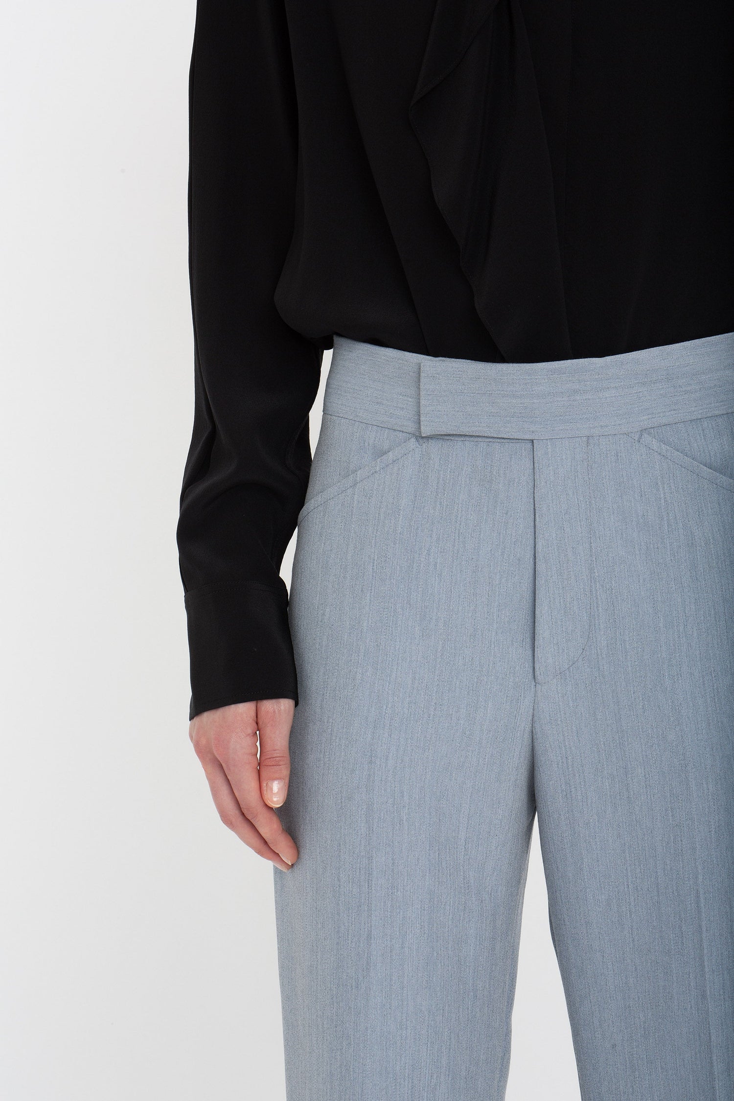 Person wearing a black long-sleeve top and light grey Victoria Beckham Exclusive Wide Cropped Flare Trouser In Marina with a flattering hint of ankle visible as their left hand rests near the trousers pocket.