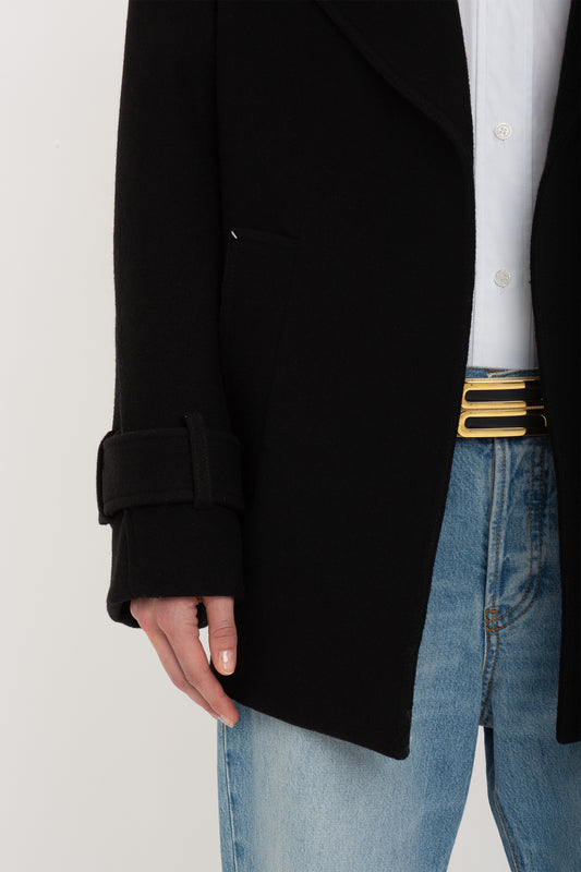 Person wearing a black Victoria Beckham Oversized Pea Coat In Black over a white shirt and blue jeans with a black and gold belt. Only the mid-section is visible.