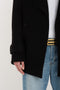 Person wearing a black Victoria Beckham Oversized Pea Coat In Black over a white shirt and blue jeans with a black and gold belt. Only the mid-section is visible.