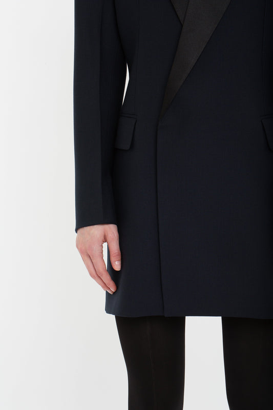 A person stands wearing a dark, long-sleeve Exclusive Fold Shoulder Detail Dress In Midnight by Victoria Beckham and black pants, reminiscent of sophisticated evening wear, with one hand visible by their side against a plain white background.