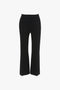 A pair of black wide-leg trousers with a high waist, front seams, and a contemporary kick hem, displayed on a white background. Designed for a leg-lengthening effect reminiscent of the Cropped Kick Trouser In Black by Victoria Beckham.