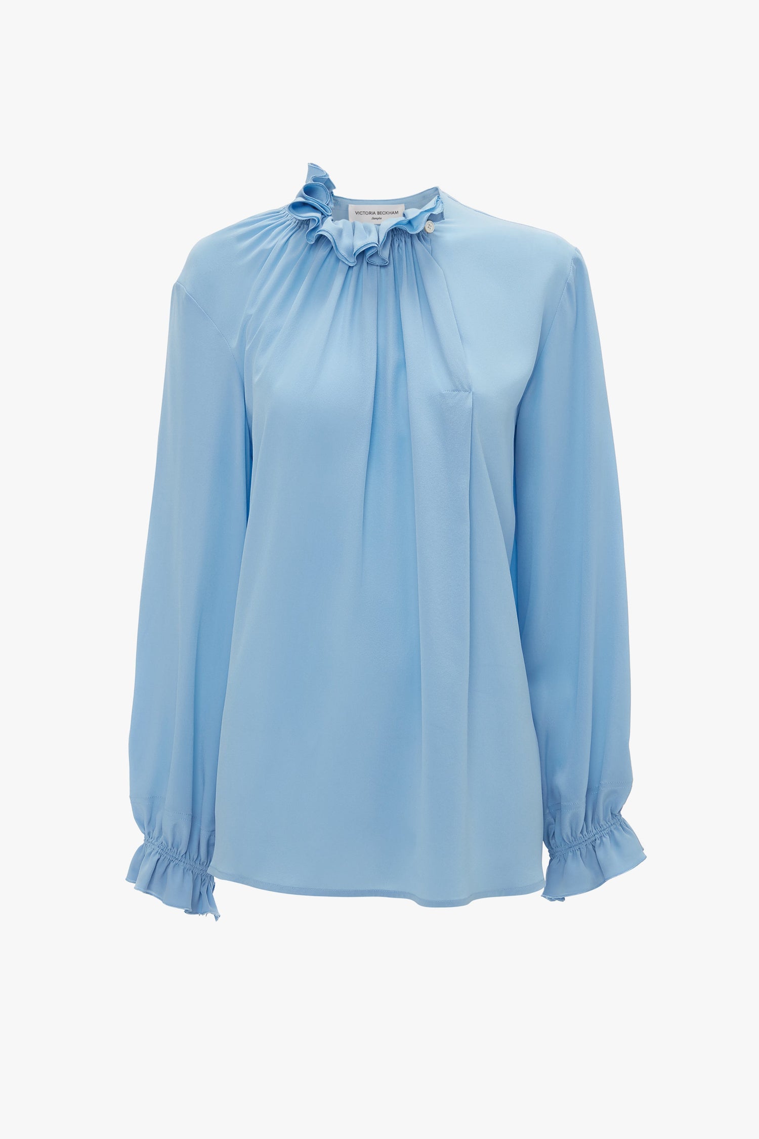 Victoria Beckham's Exclusive Ruffle Neck Blouse In Cornflower Blue features long sleeves, ruffle accents on the neckline and cuffs, and pleated detailing at the front.