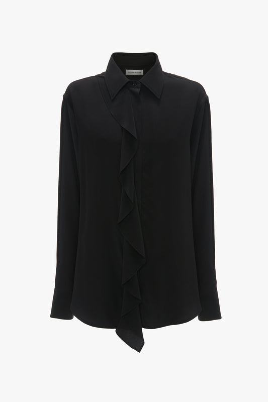 The Victoria Beckham Asymmetric Ruffle Blouse In Black is a classic black long-sleeve blouse with an asymmetric ruffle front detail and a collared neckline, crafted from fluid silk.