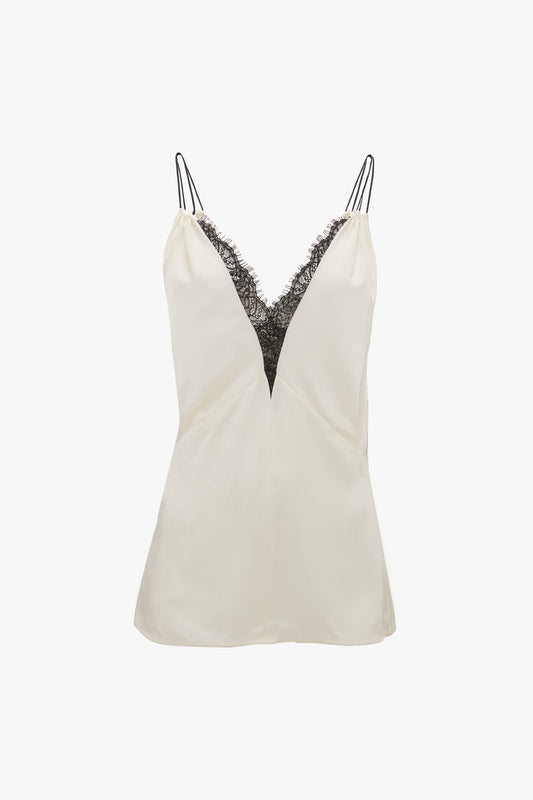 Victoria Beckham's Lace Detail Cami Top In Harvest Ivory is a light-colored crepe back satin camisole with a deep V-neckline adorned with black lace trim and thin shoulder straps, echoing the elegance of a 1990s cami top.