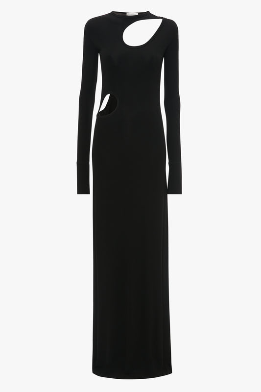 This Victoria Beckham Cut-Out Jersey Floor-Length Dress In Black is an evening gown with full sleeves, featuring a circular cutout on the upper right chest area and another cutout on the left side near the waist.