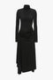 A black turtleneck dress with long sleeves, featuring a draped skirt and a high neckline - Victoria Beckham's High Neck Asymmetric Draped Dress In Black.