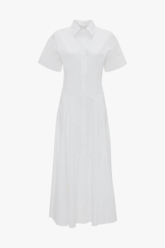 Victoria Beckham's Panelled Shirt Dress In White is a white short-sleeve, button-down dress crafted from organic cotton poplin with a collared neckline, gold button cuffs, and an ankle-length hem.
