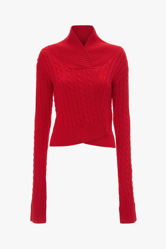 A red, long-sleeved, cable-knit sweater with a high collar and diagonal wrap design, crafted from merino wool knit for ultimate comfort, epitomizes luxury knitwear like the Wrap Detail Jumper In Red by Victoria Beckham.