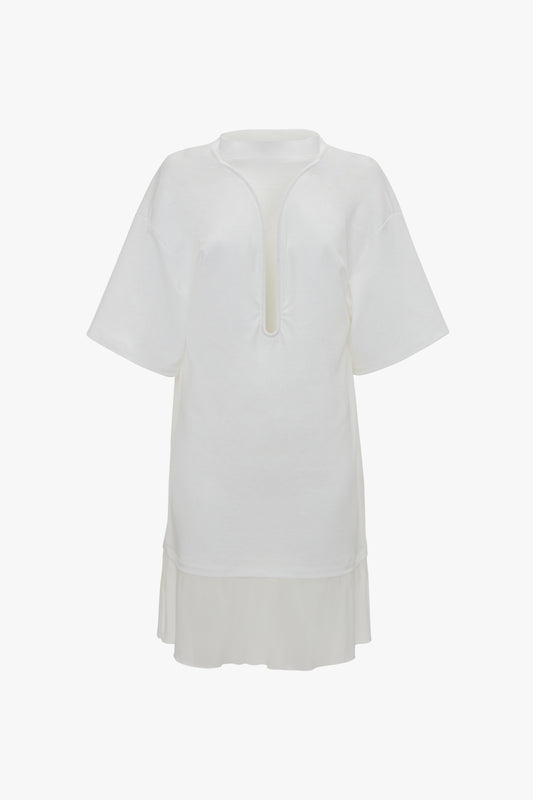 A loose, white Frame Cut-Out T-Shirt Dress In White crafted from bonded linen jersey with short sleeves and a navel-grazing keyhole neckline. The bottom features a layered hem detail for added elegance. This sophisticated piece by Victoria Beckham combines casual comfort with chic style.