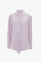 A light purple, petunia-colored Asymmetric Ruffle Blouse In Petunia by Victoria Beckham with an asymmetric ruffled front detail and a collar, offering a contemporary contrast.