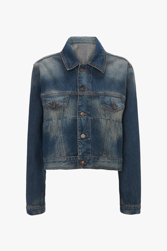 A Cropped Denim Jacket In Heavy Vintage Indigo Wash by Victoria Beckham, with long sleeves, button-up front, and two chest pockets, reminiscent of Victoria Beckham’s luxury denim style.