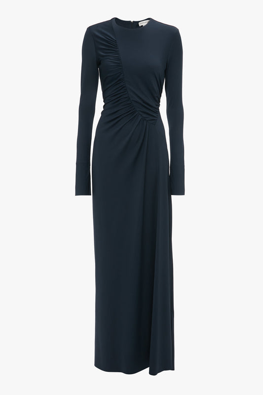 A long-sleeved, dark navy blue Ruched Detail Floor-Length Gown In Midnight by Victoria Beckham with an asymmetrical design on the front and a rounded neckline, exuding understated glamour.