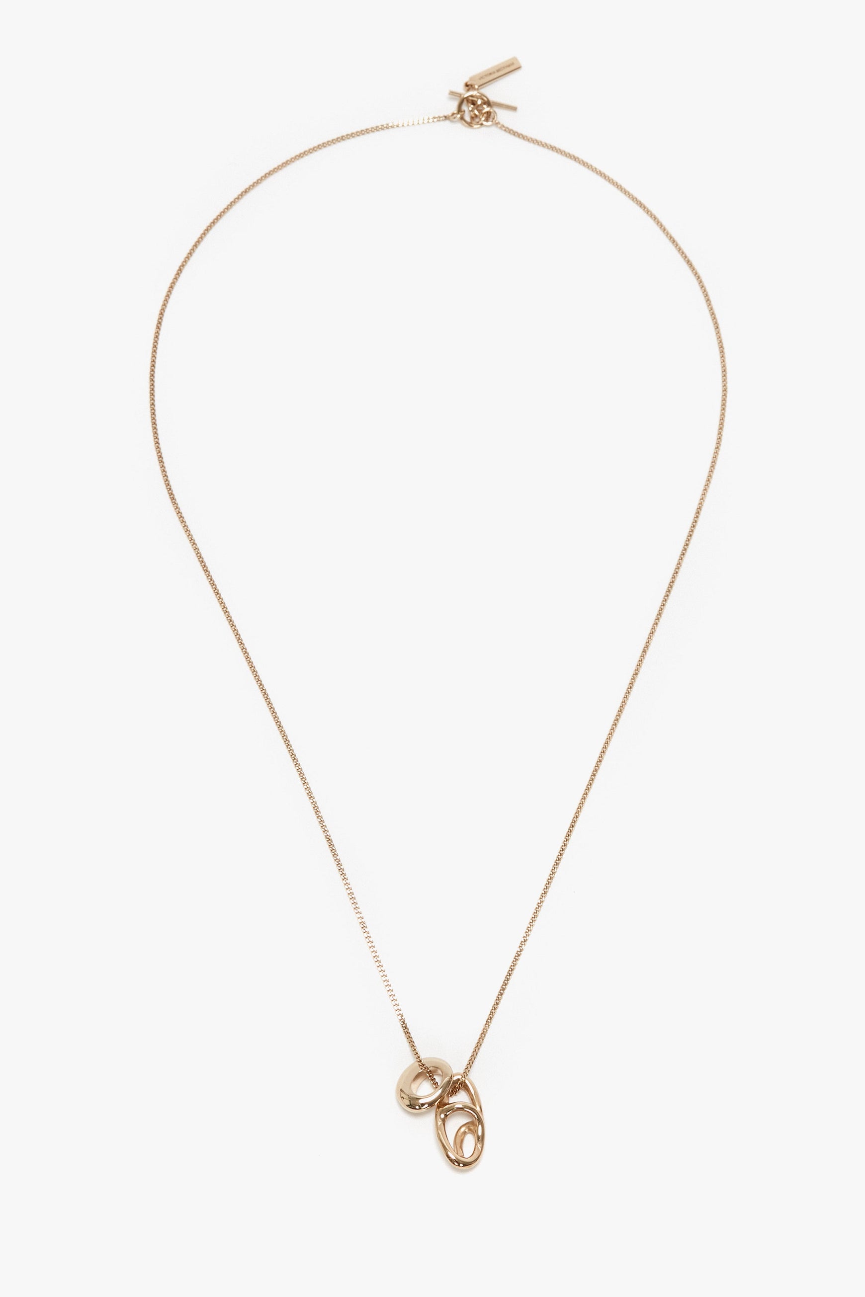 A Victoria Beckham Exclusive Abstract Charm Necklace In Light Gold featuring two linked oval pendants with a T-bar closure, displayed on a white background.