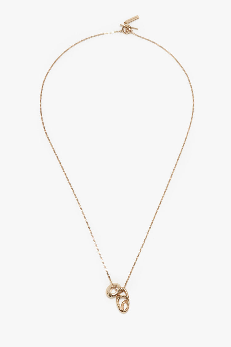 A Victoria Beckham Exclusive Abstract Charm Necklace In Light Gold featuring two linked oval pendants with a T-bar closure, displayed on a white background.