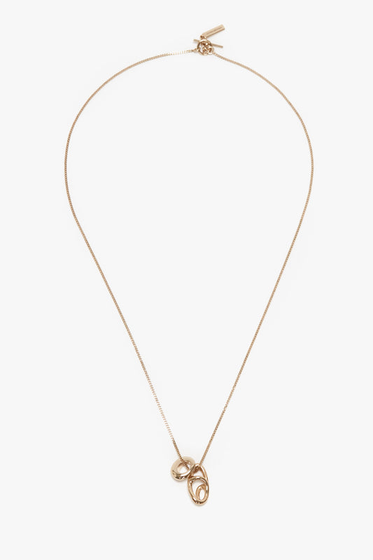 A Victoria Beckham Exclusive Abstract Charm Necklace In Light Gold featuring two linked oval pendants with a T-bar closure, displayed on a white background.