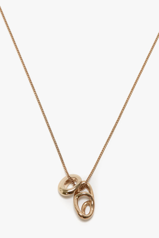 A Victoria Beckham Exclusive Abstract Charm Necklace In Light Gold with a thin chain, featuring three interlocking, oval-shaped pendants and a sleek T-bar closure.