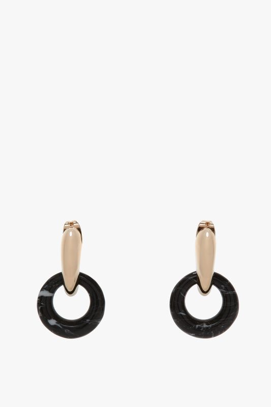 A pair of Victoria Beckham Exclusive Resin Pendant Earrings In Light Gold-Black featuring light gold-tone oval studs with dangling black ring-shaped accents and antiallergic stainless-steel closures.