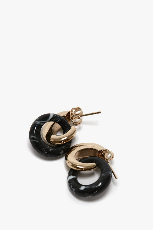 A pair of stunning Exclusive Resin Pendant Earrings In Light Gold-Black by Victoria Beckham featuring intertwined loops, one light gold and one black with a marble pattern, displayed elegantly on a white background. Complete with antiallergic stainless-steel closure for comfort.